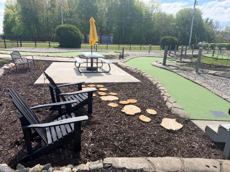 A picnic table with a yellow umbrella beside the mini golf green