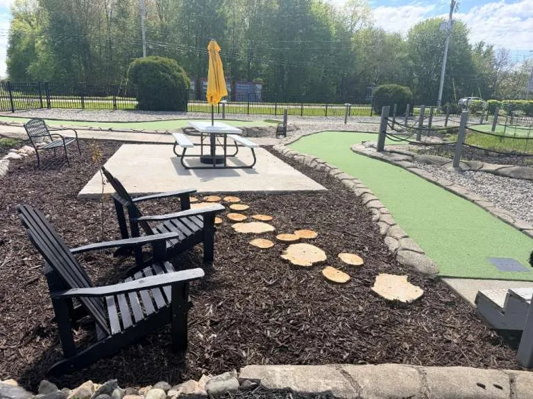A picnic table with a yellow umbrella beside the mini golf green